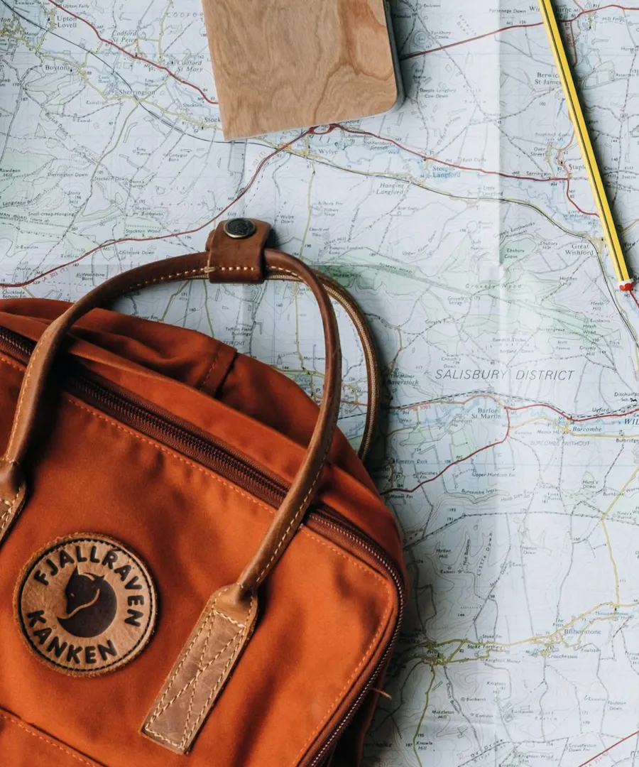 Un sac de voyage orange posé sur une carte routière, à côté d'un carnet et d'un crayon