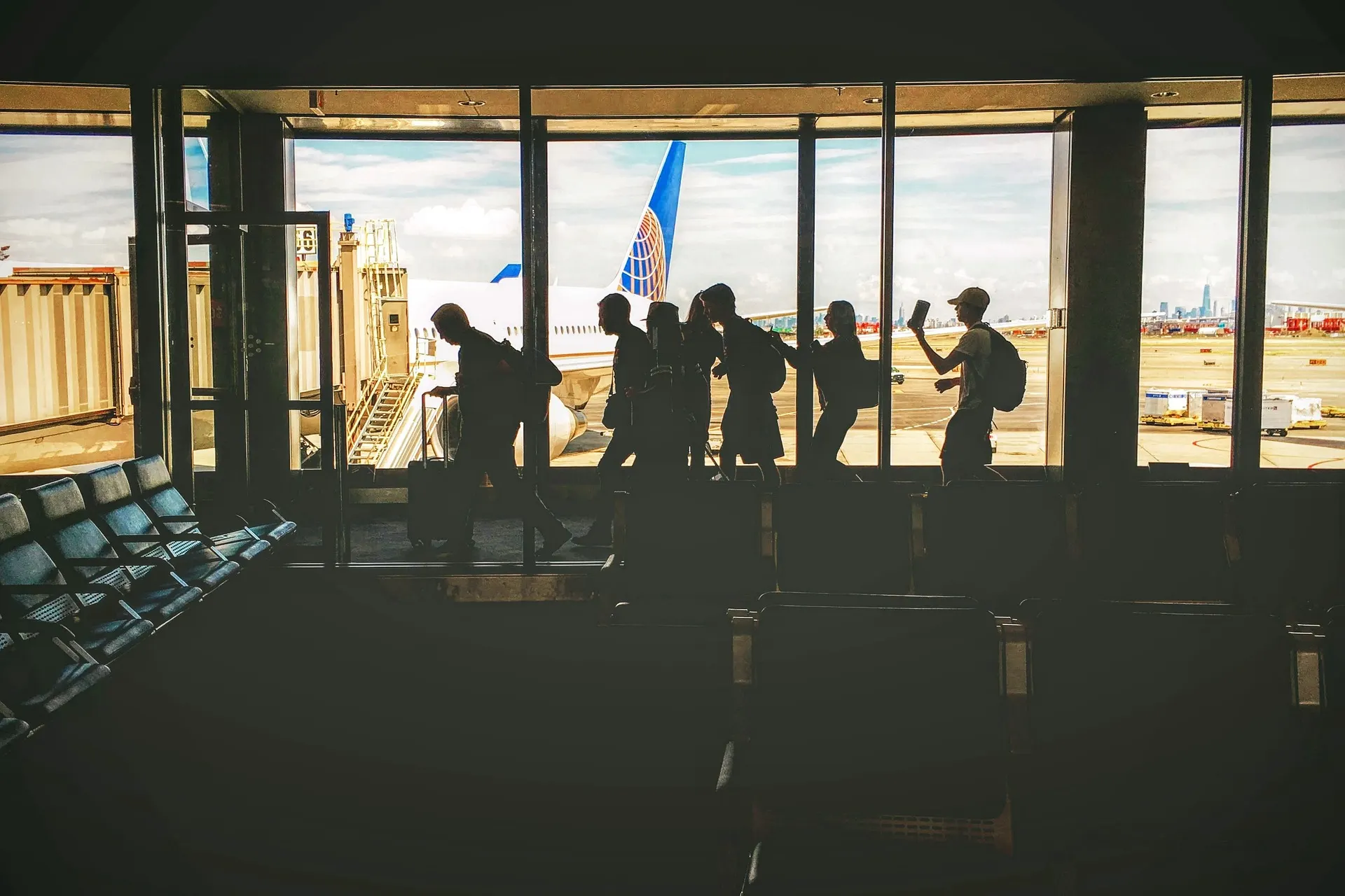 Silhouettes d'un groupe de voyageurs qui longe les baies vitrées d'un aéroport